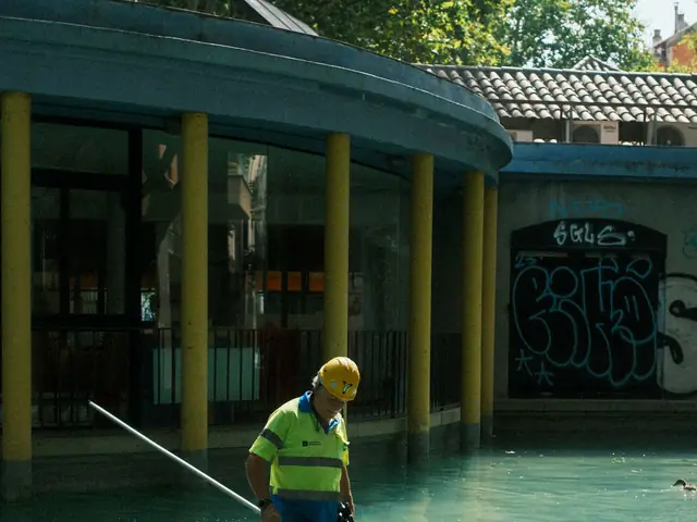 A pool maintenance worker, seen from behind, cleaning an outdoor pool with a net.